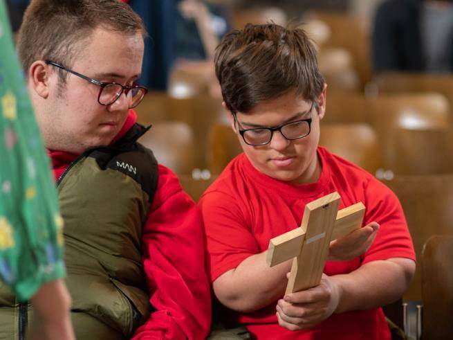 Child handles wooden cross with adult alongside