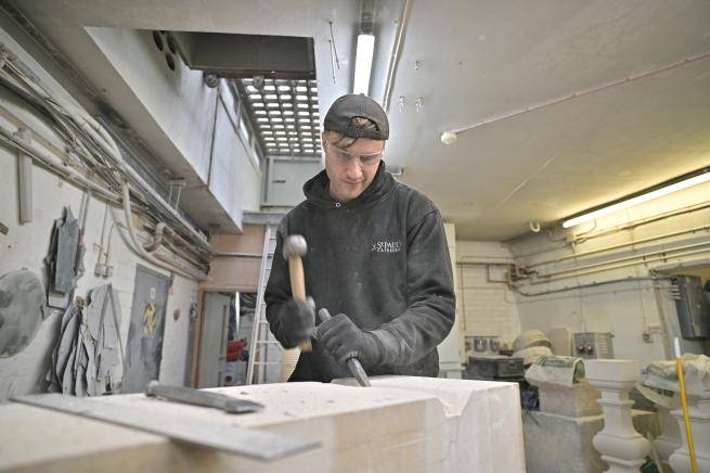 stonemason using a hammer and chisel to carve a large stone inside a workshop
