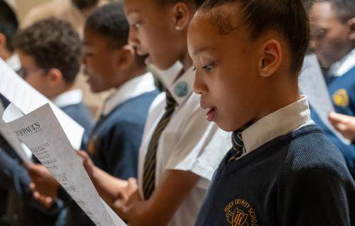 girls and boys in school uniform singing from sheet music