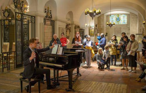 Man at piano directing parents and children