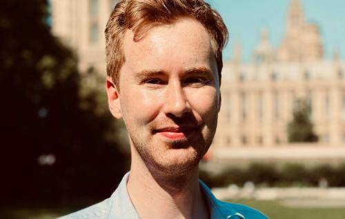 James Roberts, a white male wearing a blue shirt with collar standing in front of a cathedral