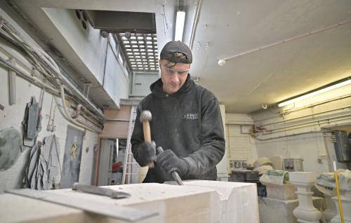 stonemason using a hammer and chisel to carve a large stone inside a workshop
