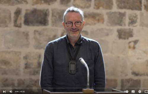 Martin stands at a microphone in the Wren Suite