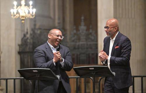 Two black men are standing on a stage in the Cathedral and laughing as they converse